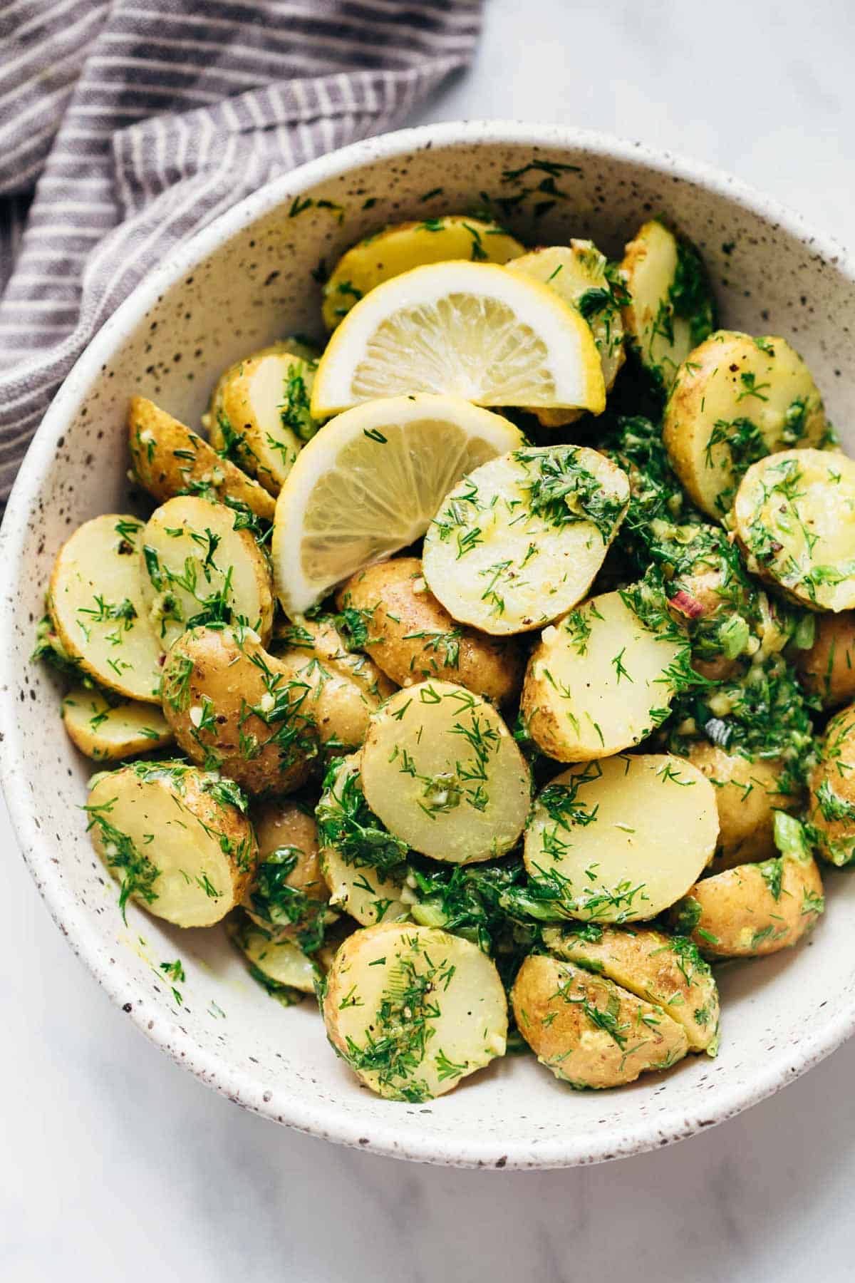Healthy Lemon Dill Potato Salad (no mayo) served in a white speckled bowl with lemon wedges