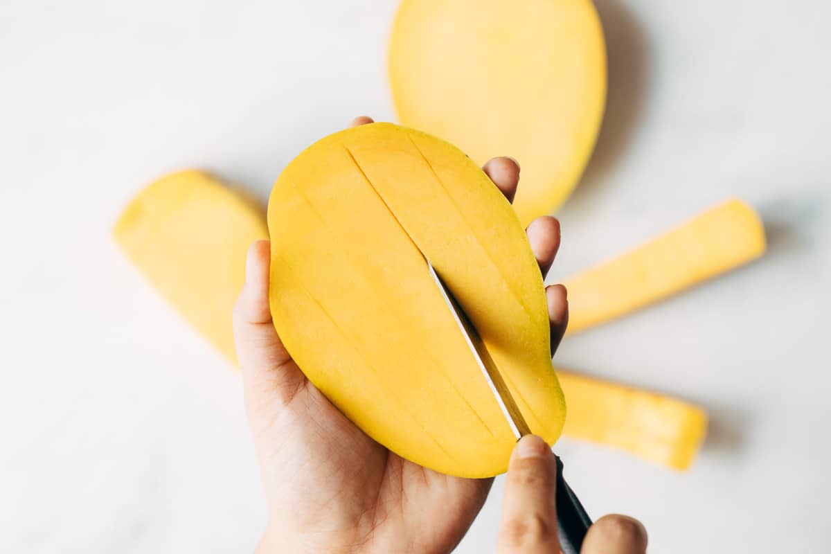 Vertical cuts being made on a mango to cut it into dices.