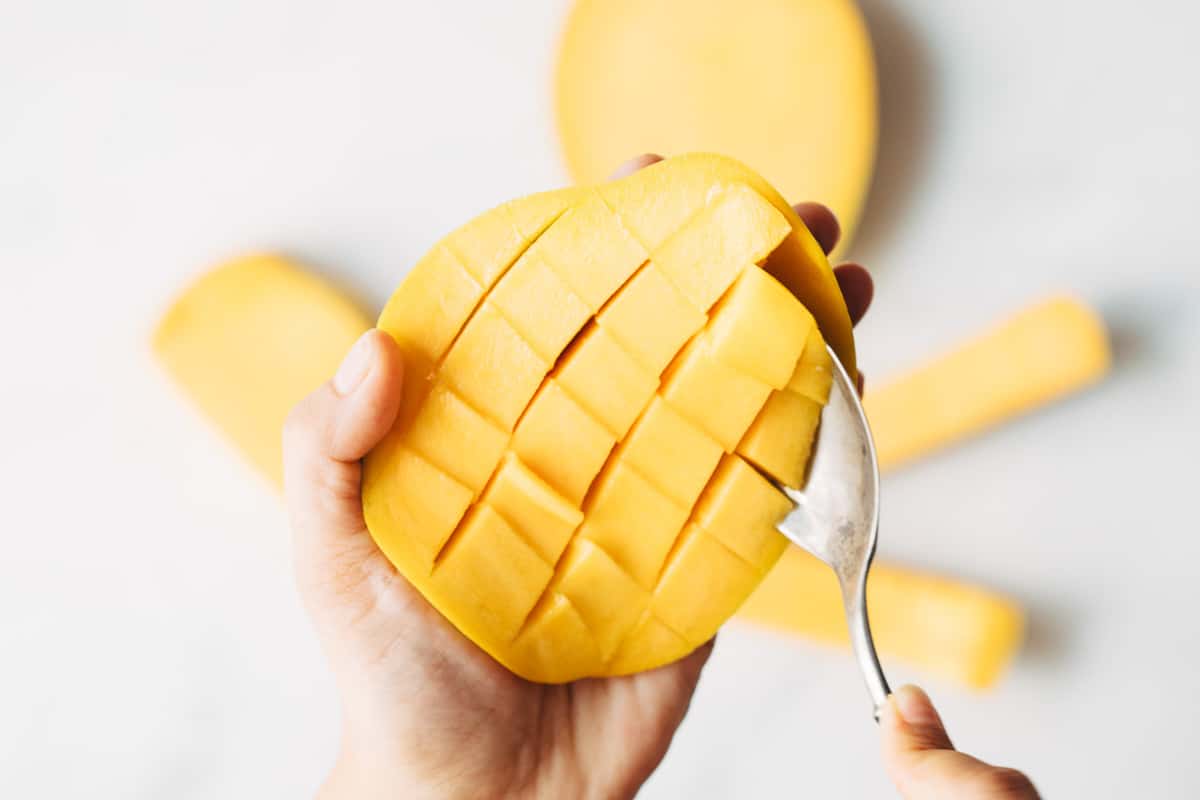 An unpeeled mango cut into dices being spooned out.