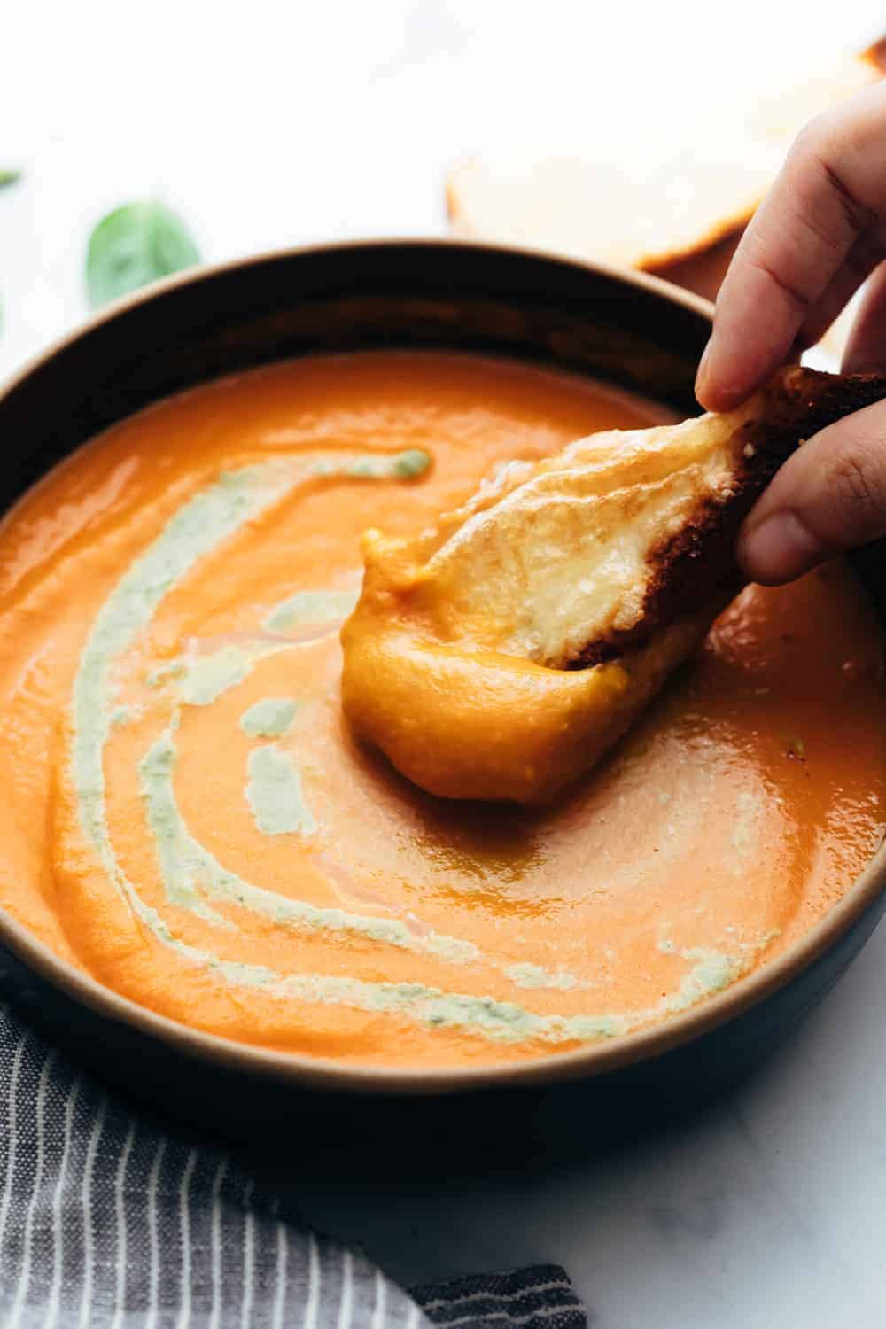 Roasted Tomato Pesto Soup served in a bowl with cheesy bread being dunked into soup