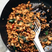 thai basil chicken being in cooked in a wok with a steel spatula