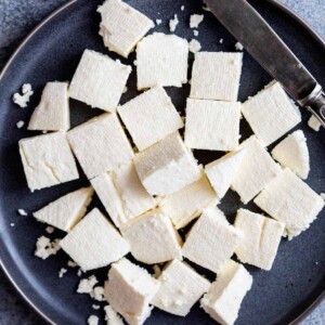 Cubes of paneer served on a grey plate with a knife