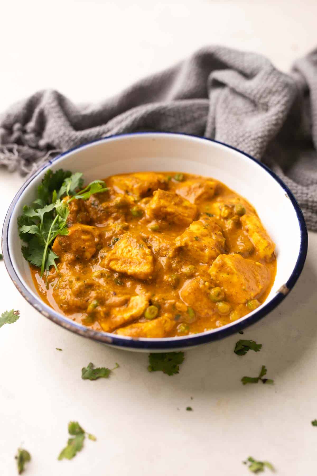 shot of matar paneer gravy in a white bowl with coriander sprinkled on top