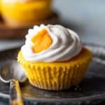 Mini mango cheesecakes served on a plate topped with whipped cream and fresh mangoes