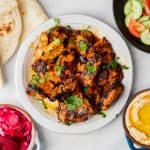 Chicken Shawarma laid out on a table along with pita, hummus, veggies, pickled beets and onions