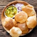 Pooris served on a plate with aloo bhaji, onions