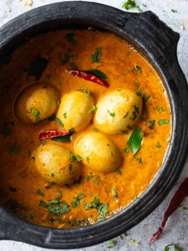 an image of south indian style egg curry in a black clay pot and garnished with coriander and curry leaves