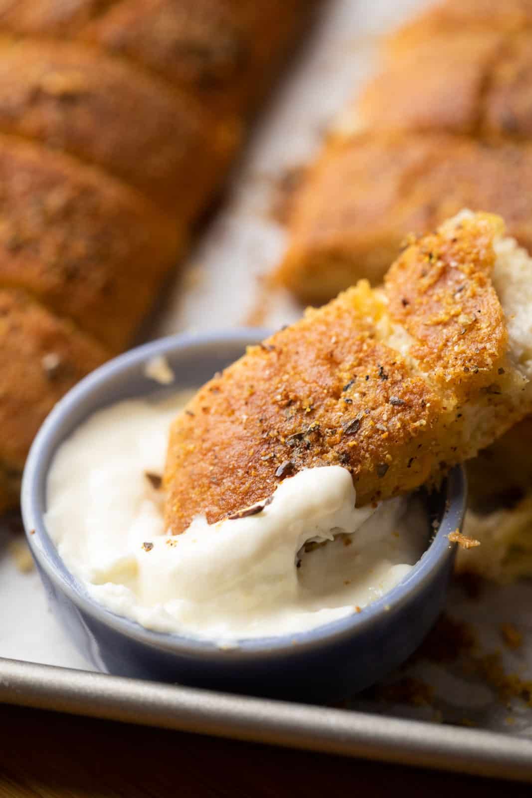 Closeup of a breadstick dipped in cheese sauce