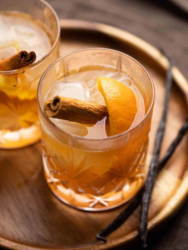 A glass of vanilla cinnamon old fashioned on a tray with vanilla beans on the side
