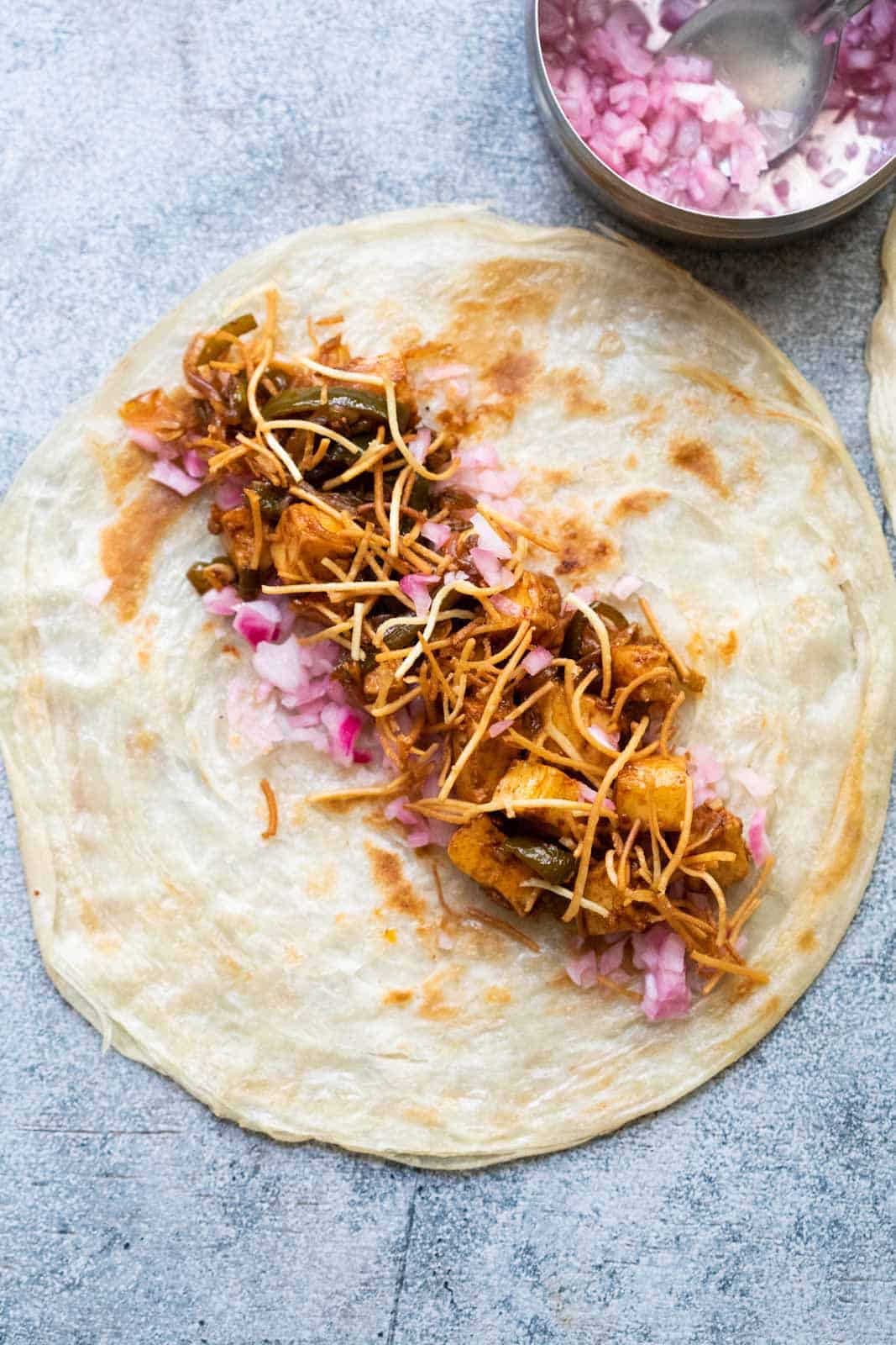 A paratha laid out on the worktop with paneer filling and crispy noodles in it