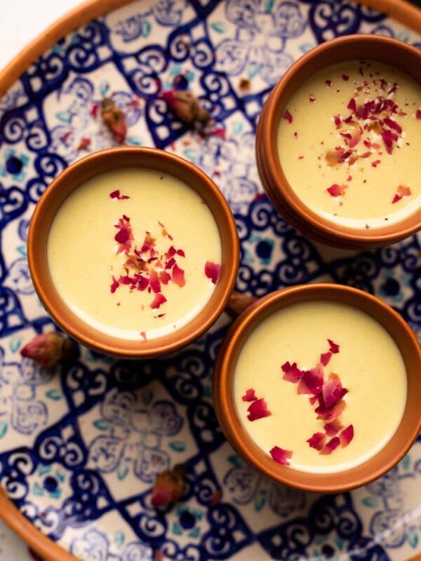 Thandai served in three mud glasses served on a colourful blue plate with rose petals on top