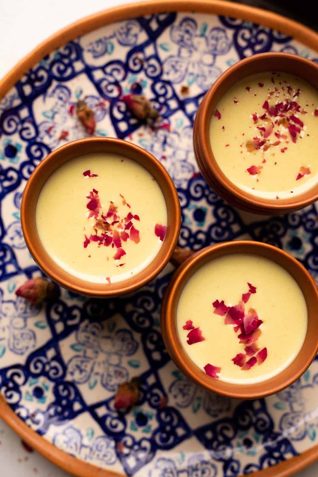 Thandai served in three mud glasses served on a colourful blue plate with rose petals on top