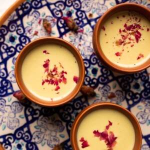 Thandai served in three mud glasses served on a colourful blue plate with rose petals on top