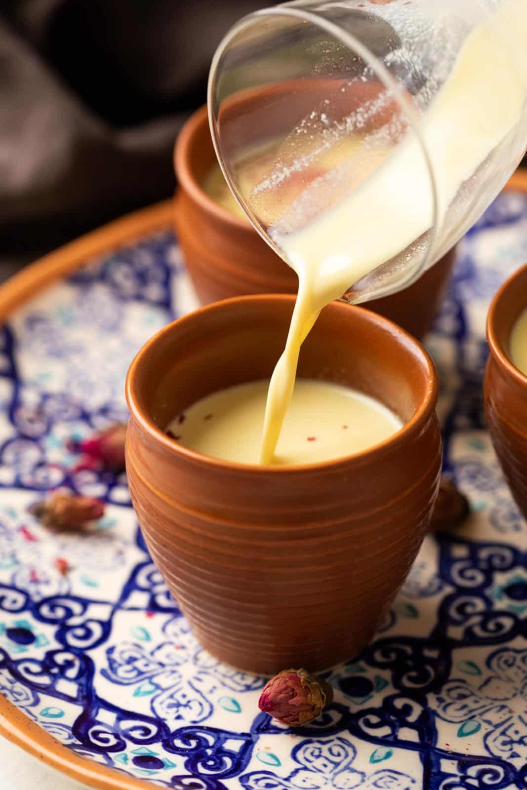 Thandai being poured from a glass jar into mud glasses or kullads