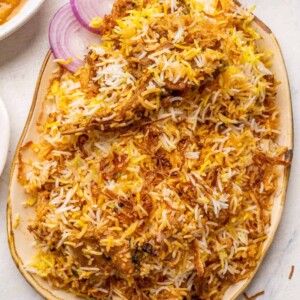 Mutton biryani served on a platter with sliced onions, raita and mirchi salan