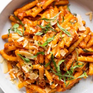 Pasta in red sauce topped with shaved parmesan and basil served in a grey white bowl with a fork on the side