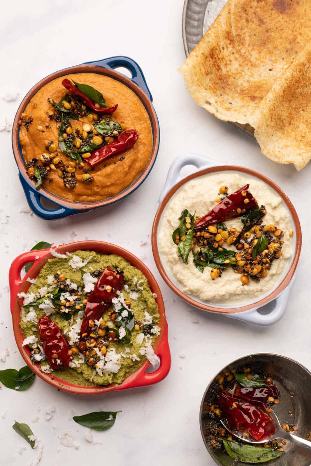 3 south indian chutneys served in bowls with two dosas on the side