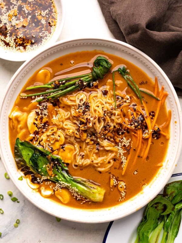 A bowl of vegetarian ramen topped with chives and bok choy and served with sesame chilli oil on the side