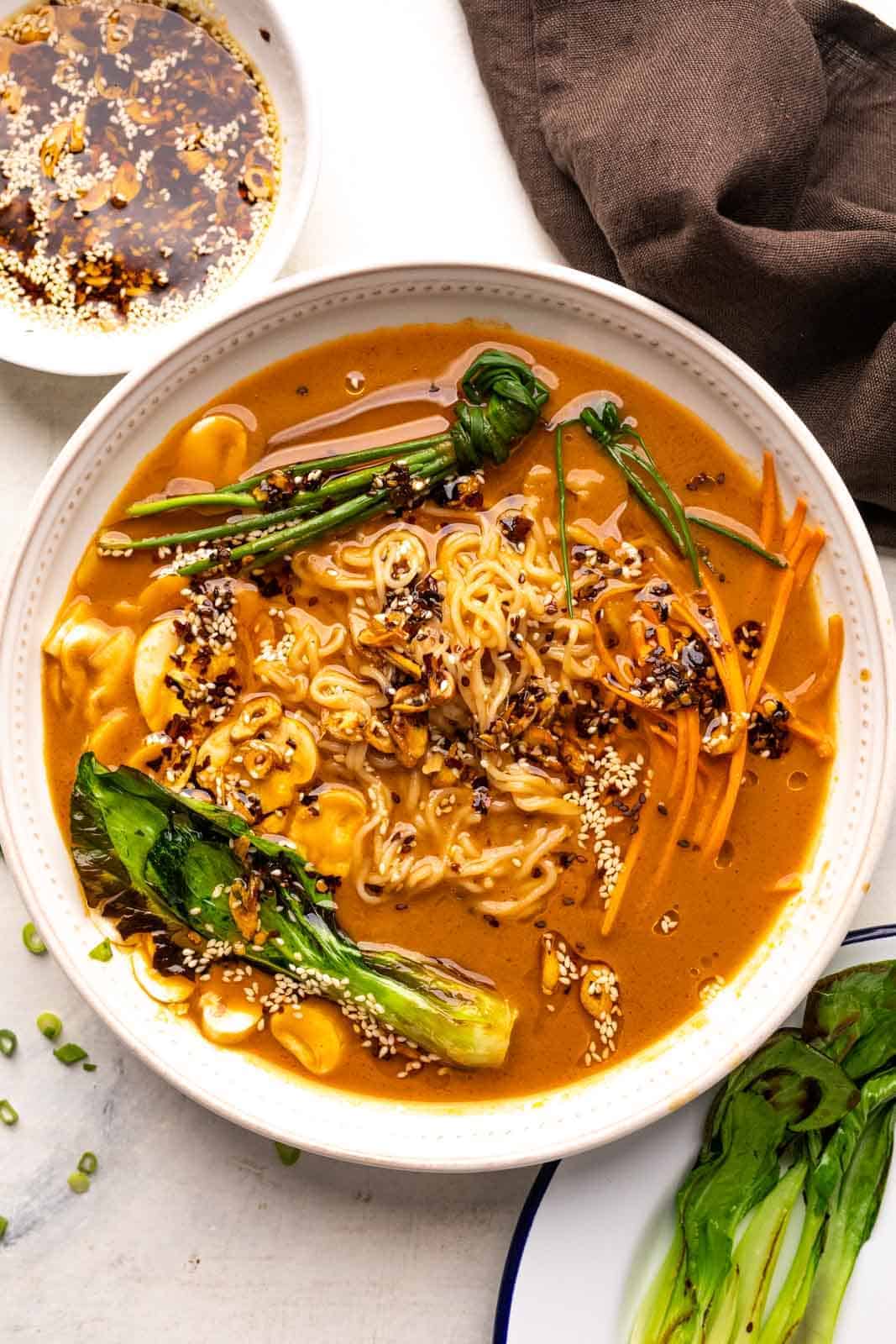A bowl of vegetarian ramen topped with chives and bok choy and served with sesame chilli oil on the side