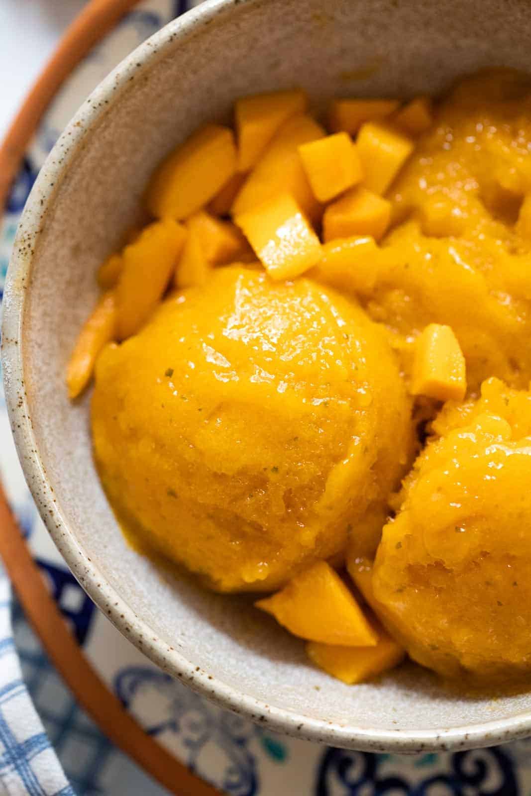 Mango sorbet scoops served in a brown ceramic bowl with diced mangoes