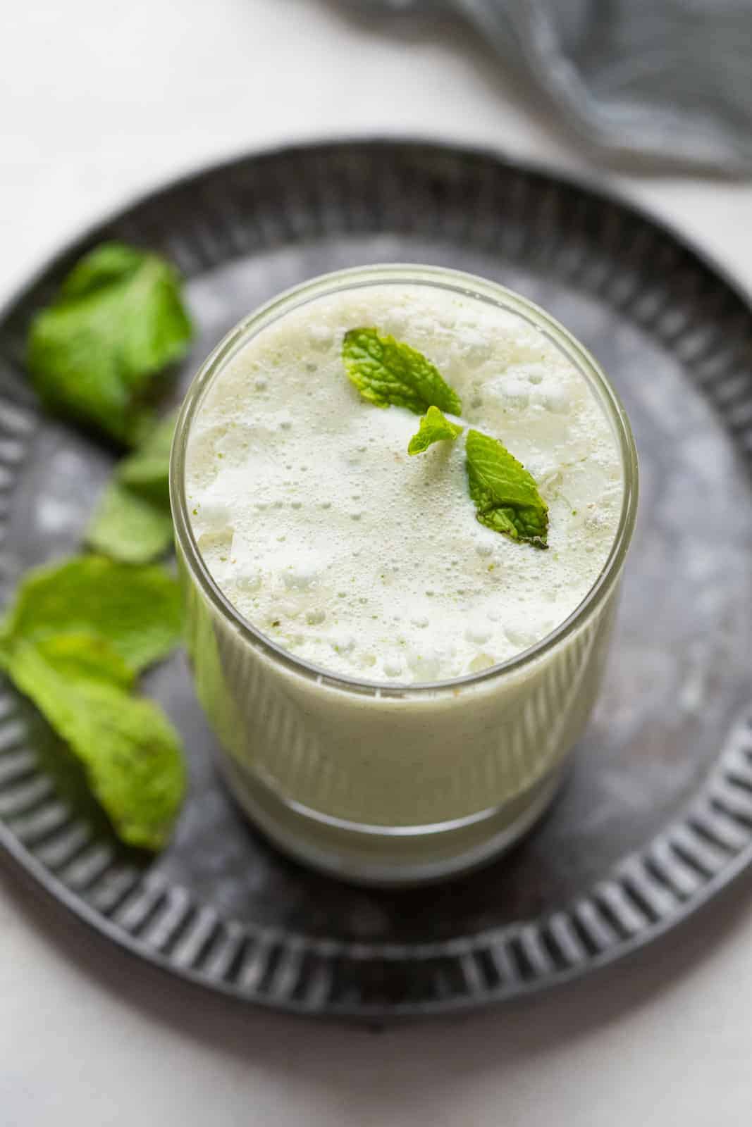 pudina chaas with ice cubes served in a glass on a metal tray