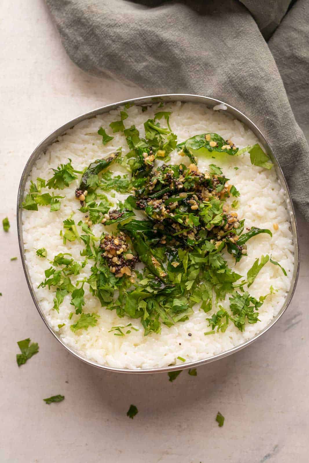 Curd rice set in a steel bowl topped with tempering and chopped coriander