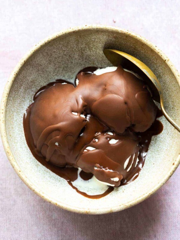 Chocolate magic shell that has hardened over vanilla ice cream to form a crackly crispy shell served in a brown ceramic bowl with a spoon