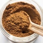 Garam Masala pictured in a glass jar used for storage with a spoon in it