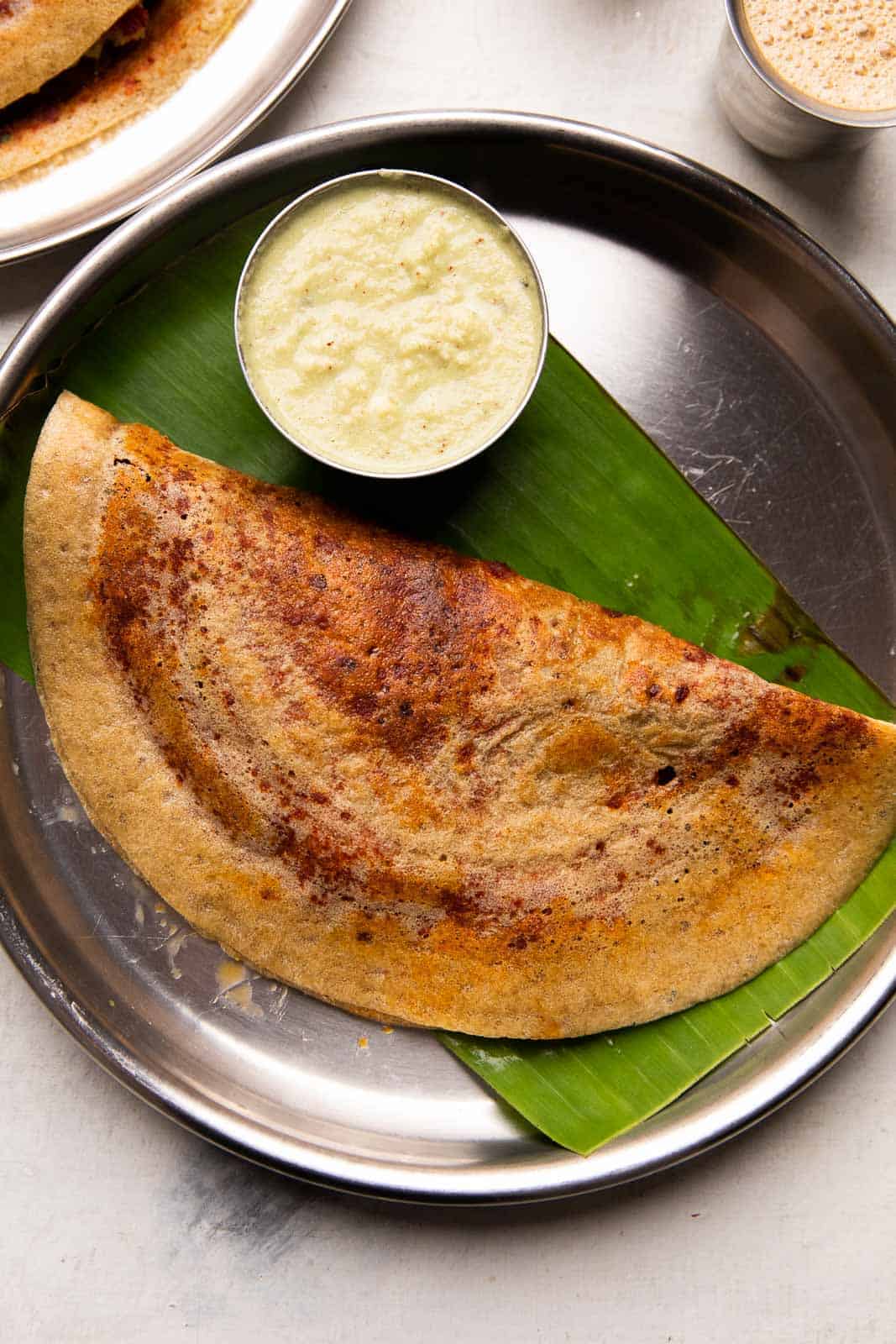Millet mysore masala dosa served on a steel plate with chutney and filter coffee