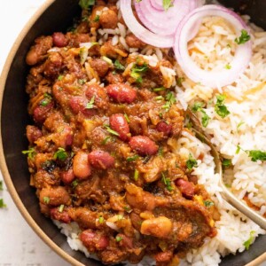 Rajma Masala served in a bowl on top of rice with sliced onions on the side