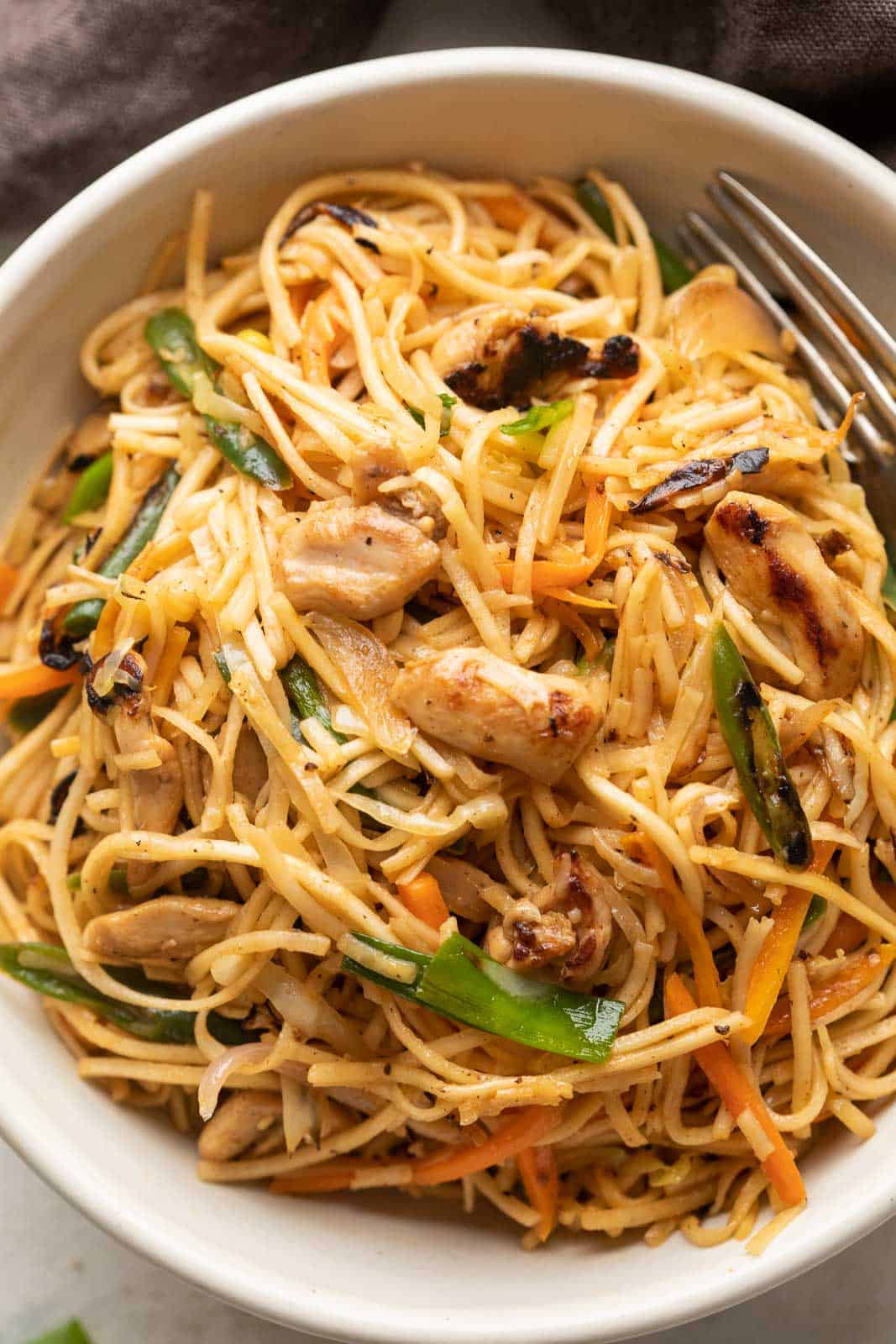 Chicken Chow mein served in a white bowl with a fork on the side