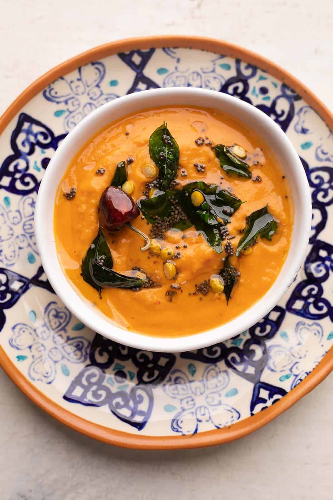 South Indian style tomato chutney or thakkali chutney served in a white bowl on a blue and orange plate with tempering on top