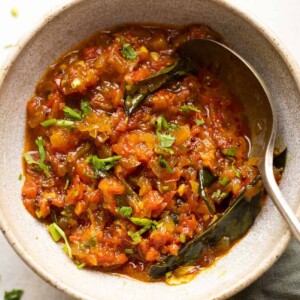 North Indian style tomato chutney served in a ceramic bowl with a spoon on the side