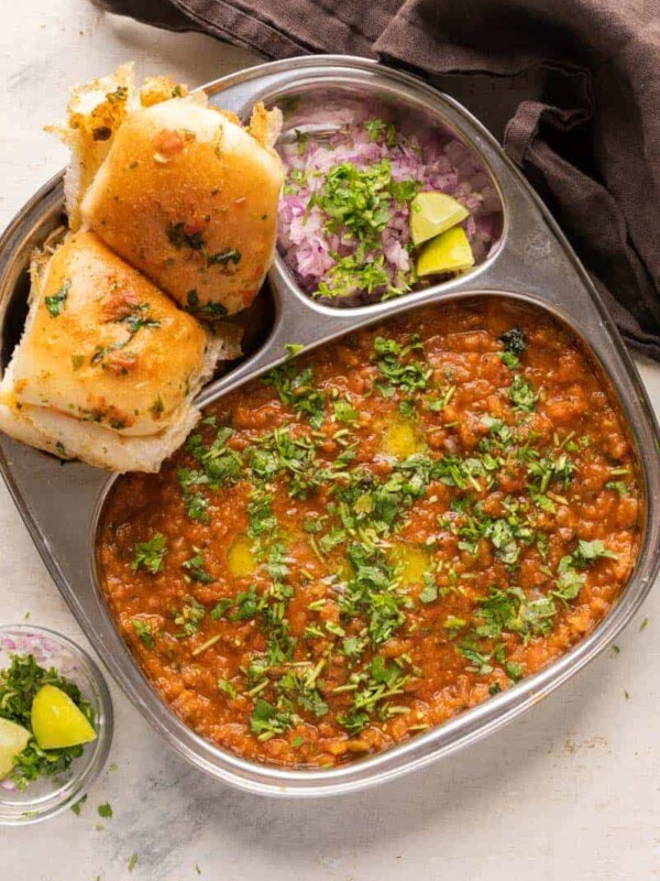 Pav Bhaji served in a steel plate with ladi pav, onions and coriander on the side