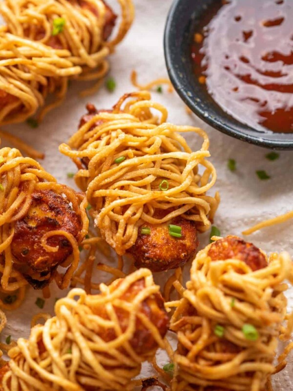 Thread paneer served on tissue paper lined plate with sweet chilli sauce on the side