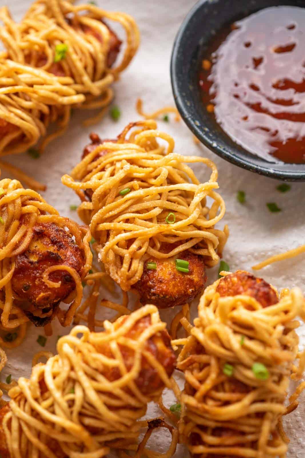 Thread paneer served on tissue paper lined plate with sweet chilli sauce on the side