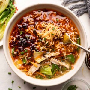 Chicken thukpa served on a white bowl with a fork twirling around noodles and bok choy on the side