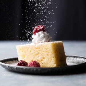 Eggless Vanilla Cake served on a plate with whipped cream and raspberries and a dusting on sugar