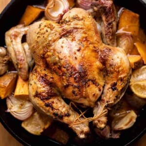 Herb garlic roast chicken served on a bed of roasted vegetables in a cast iron pan