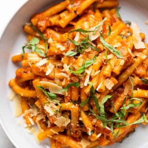 Red sauce pasta made in an instant pot served in a white bowl with shaved parmesan and chopped basil on top