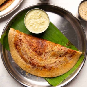 Millet Dosa served on a banana lead lined steel plate with chutney and filter coffee