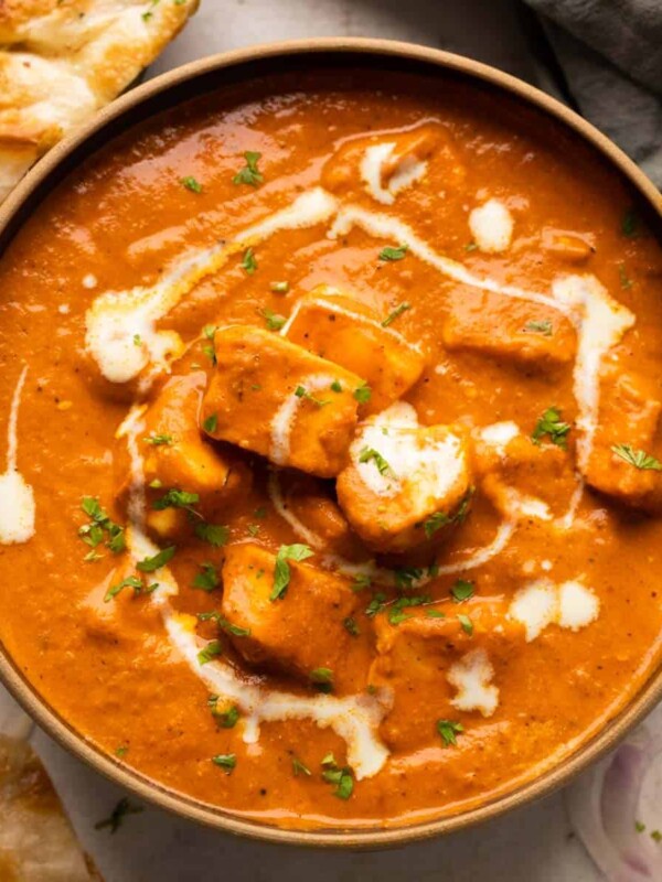 Paneer Butter Masala served in a brown bowl with naan and onions on the side