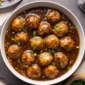 Veg manchurian served in a white bowl with fried rice and spring onions on the side