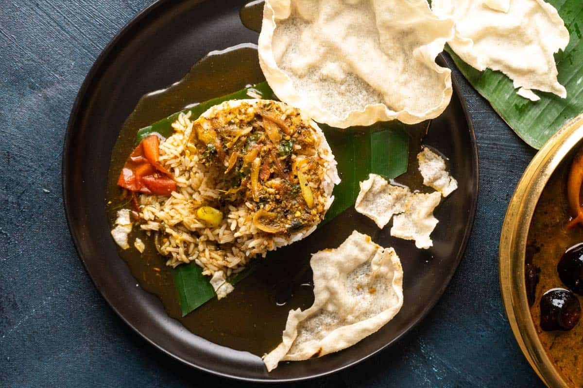 Picture of rasam poured over a mound of rice with papad on the side