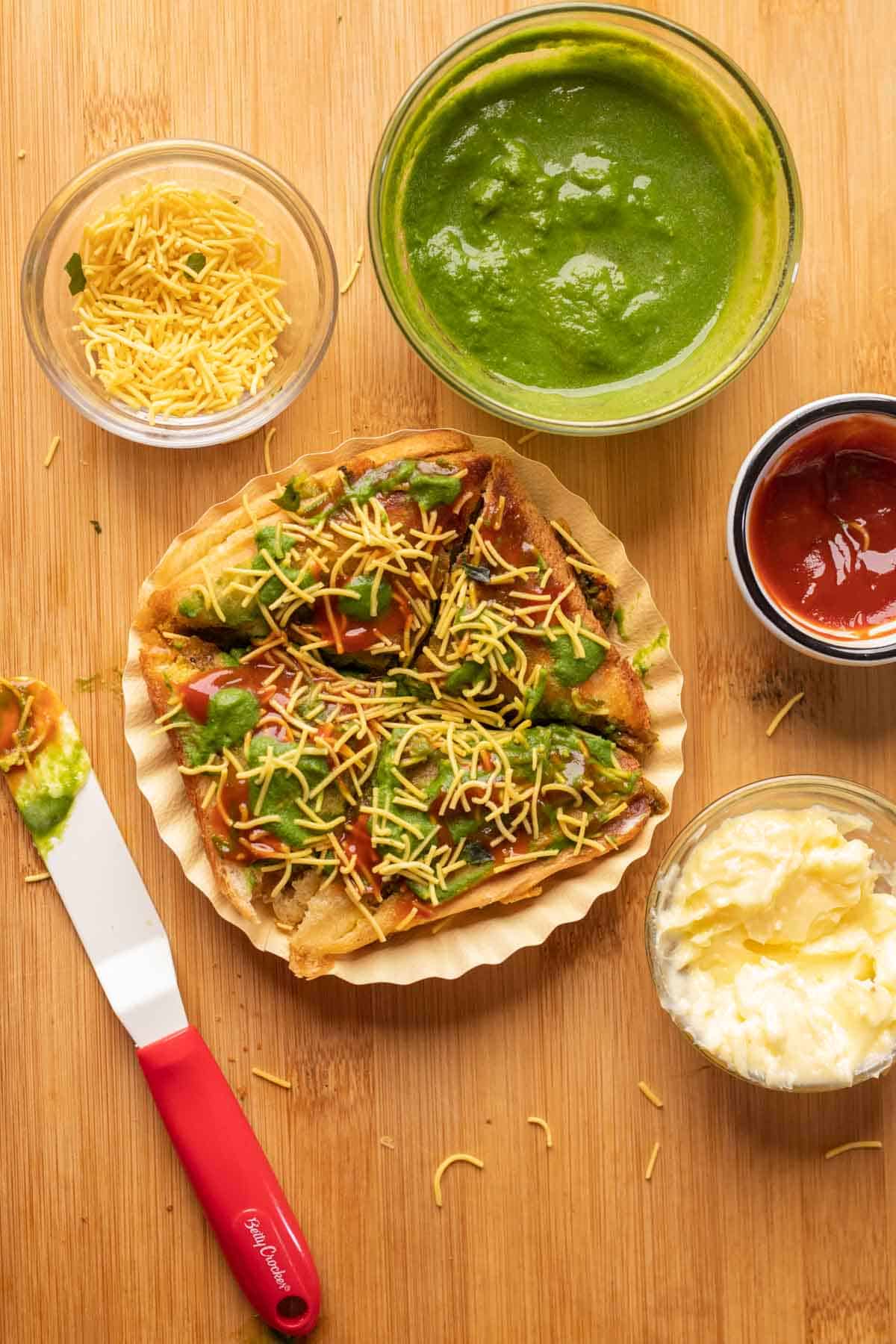 Toasted sandwich topped with butter, chutney, ketchup and sev served on a paper plate