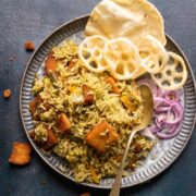 Rice bath served in a grey plate with fryums, poppdum and onions on the side