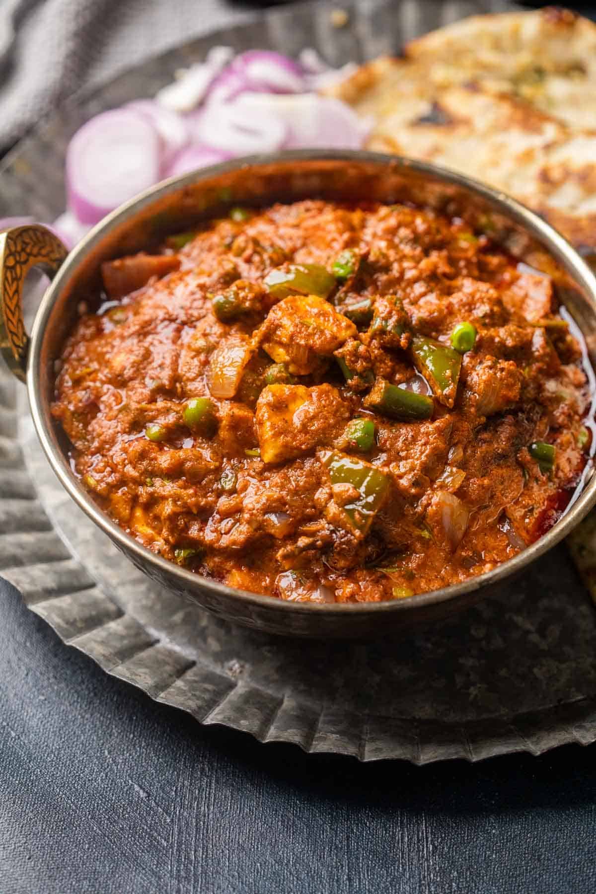 Picture of veg kolhapuri served in a copper kadhai on a plate with onions and naan