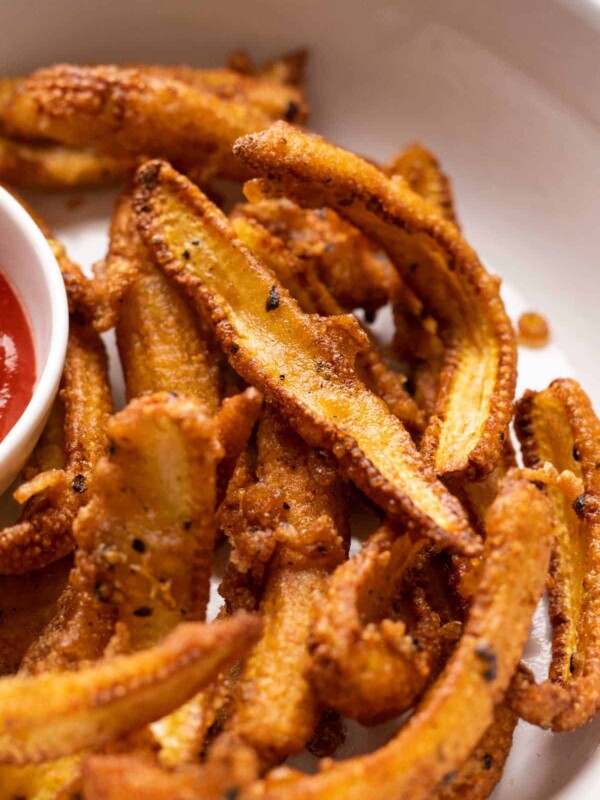 Closeup of crispy baby corn fry served in a white plate with ketchup on the side