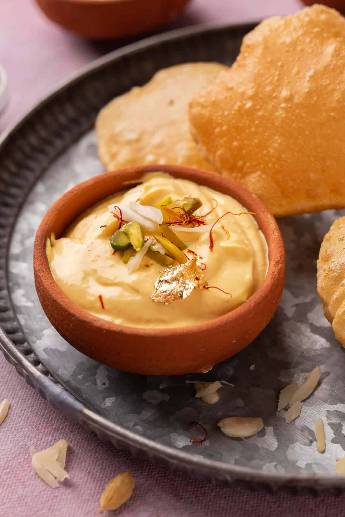 Mango Shrikhand served on a plate with pooris