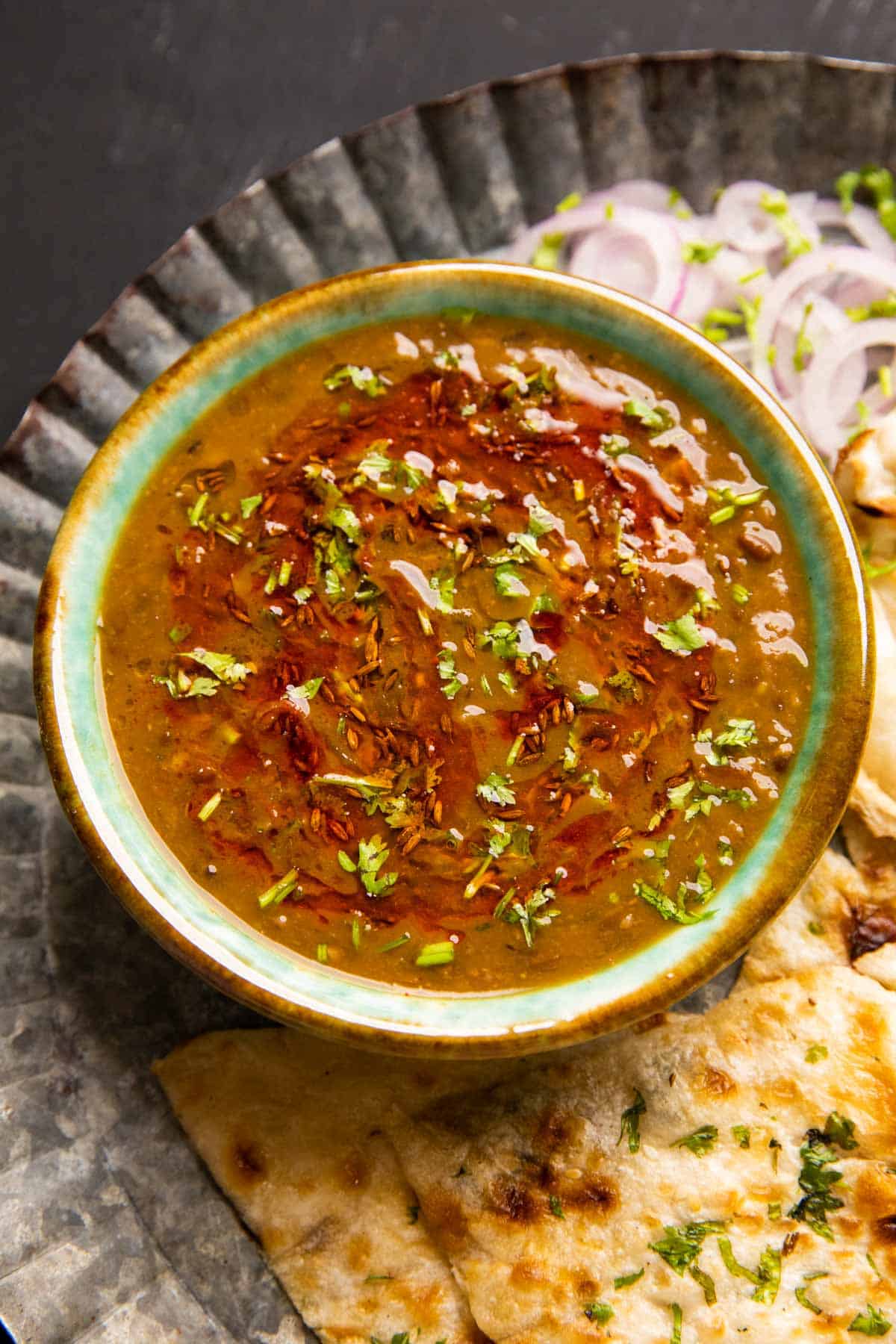 Langar wali dal served in a green ceramic bowl with naan and onions on the side